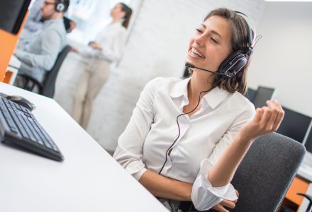 Beautiful young customer support female operator talking with client via hands-free headset in call center